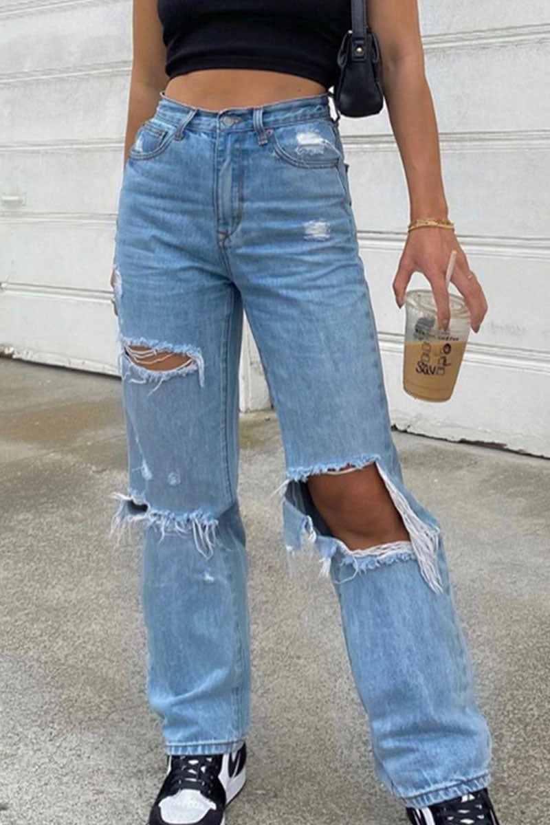 Person wearing ripped blue jeans holding a coffee cup against a plain background