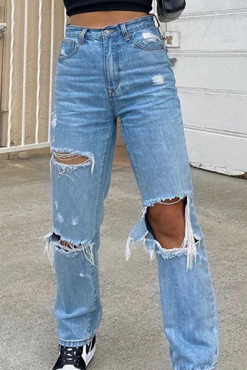 Ripped blue jeans worn by a person on a concrete surface.