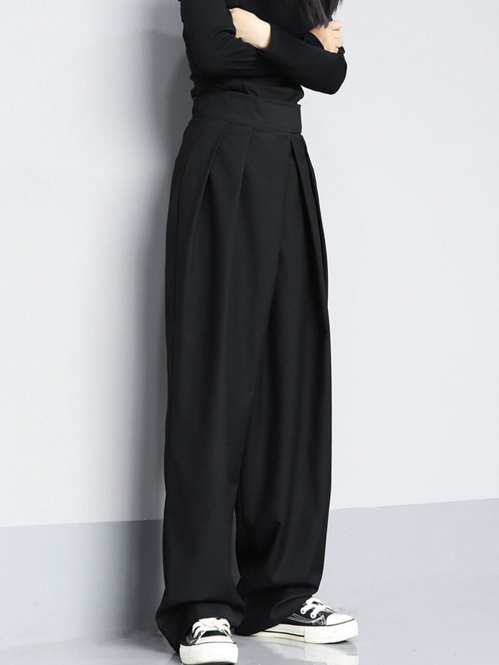 Person wearing black wide-leg pants and black shoes against a plain background