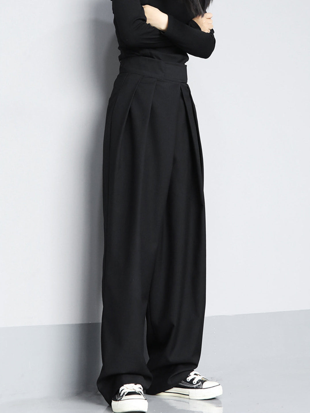 Person wearing black wide-leg pants and black shoes against a plain background