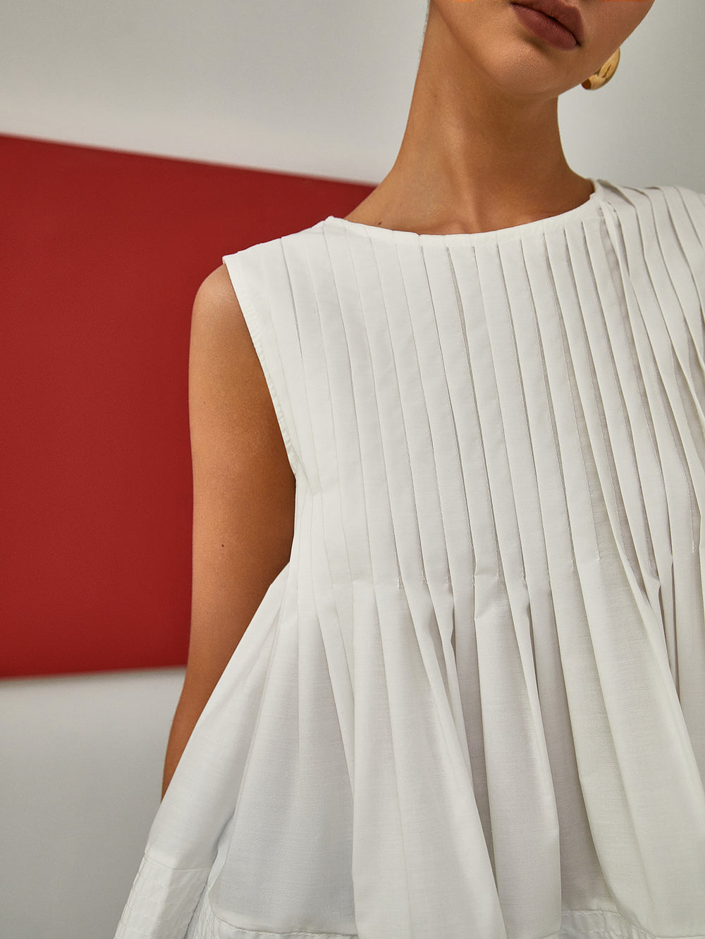White pleated dress worn by a person with a red and gray background