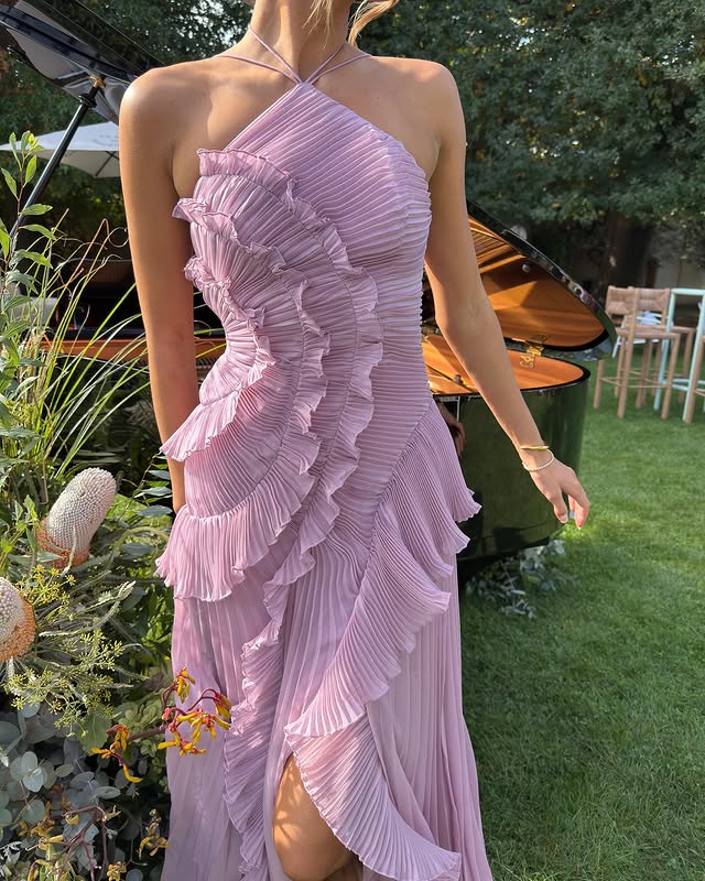 Woman wearing a pink ruffled dress outdoors with greenery and furniture in the background