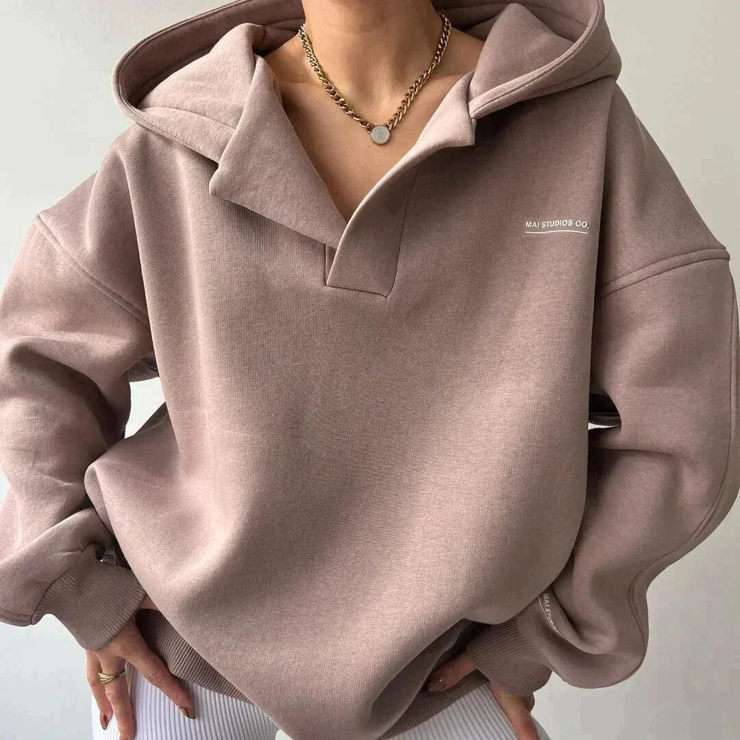 Person wearing a light brown hoodie with a brand logo on a neutral background