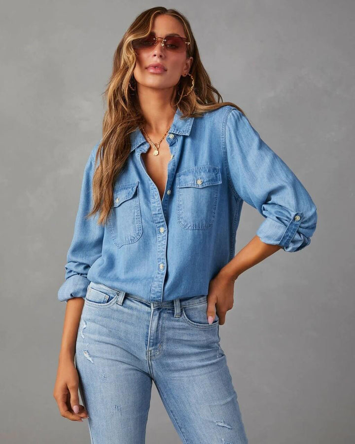 A woman wearing a relaxed fit denim button-up shirt with chest pockets and rolled-up sleeves, paired with jeans and sunglasses.