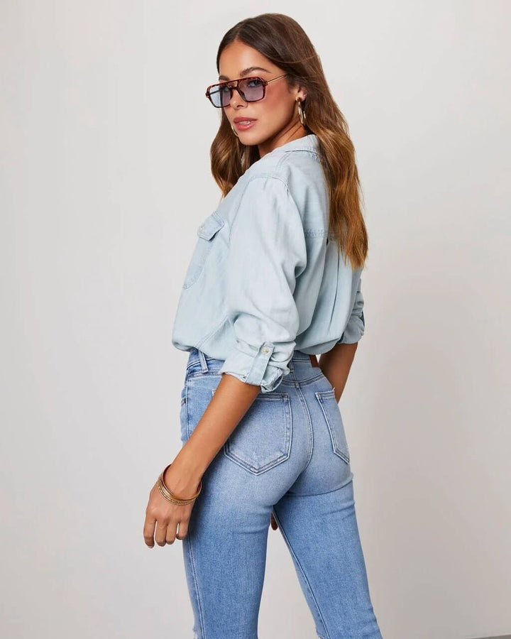 Person wearing a light blue denim jacket and jeans against a plain background