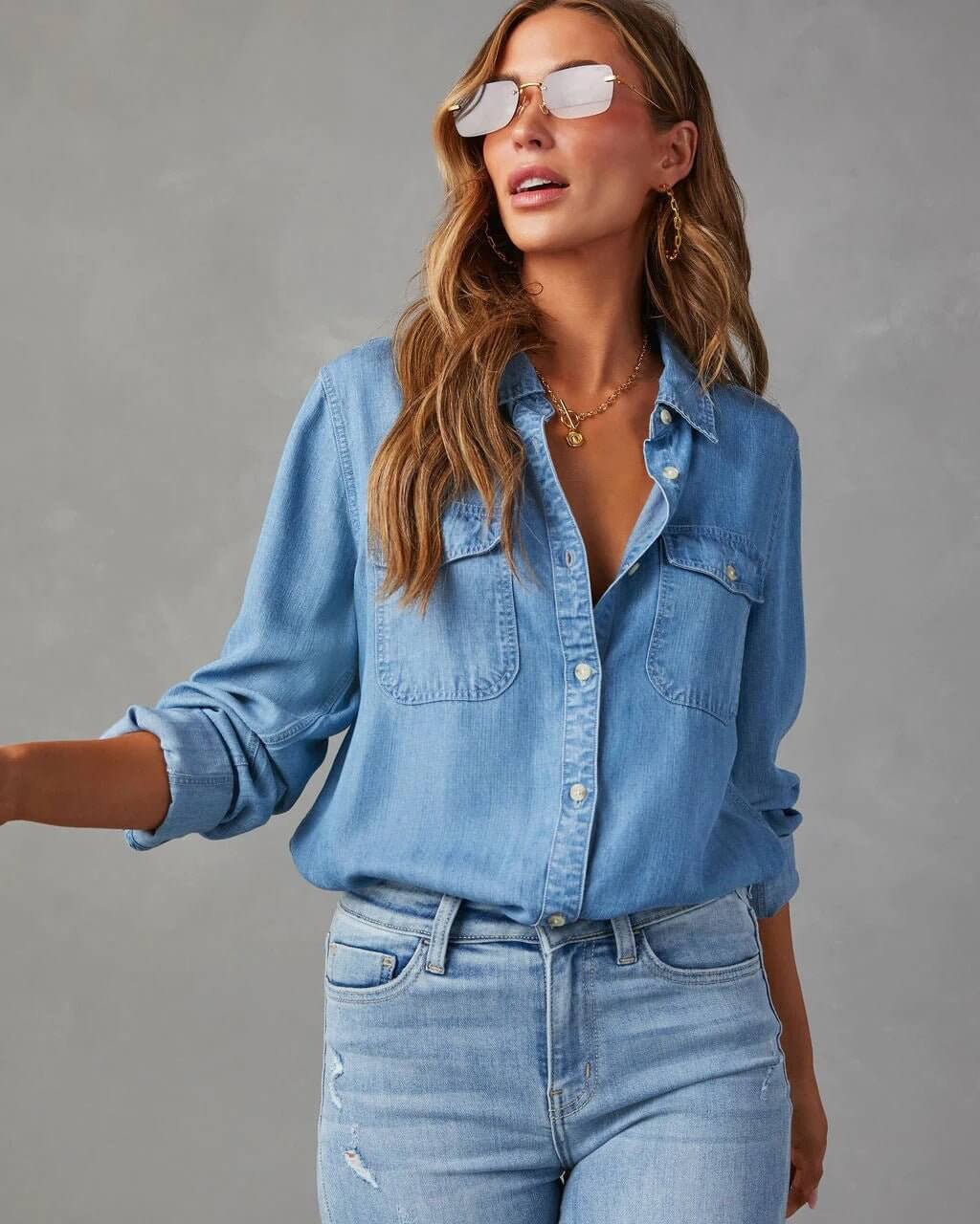 Woman wearing a denim shirt and jeans against a gray background