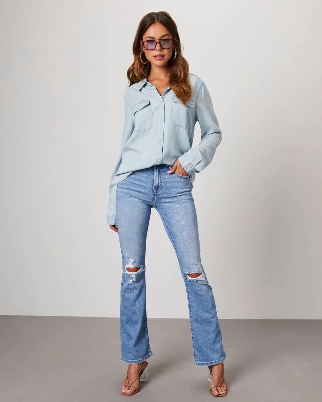 Woman wearing light blue denim shirt and jeans against a plain background