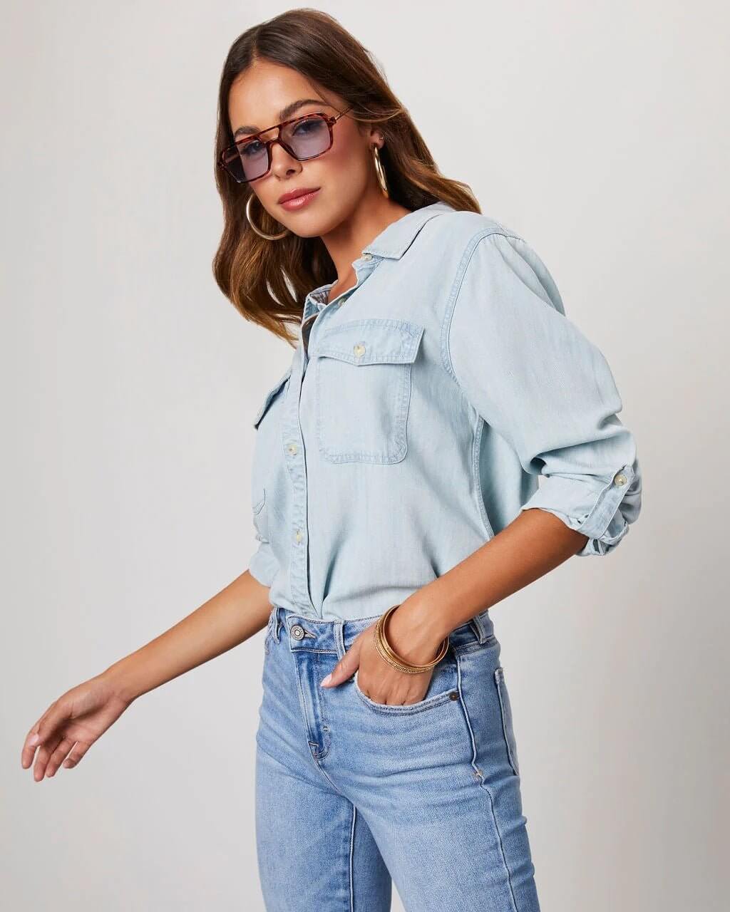 Person wearing a light blue denim shirt and jeans against a plain background